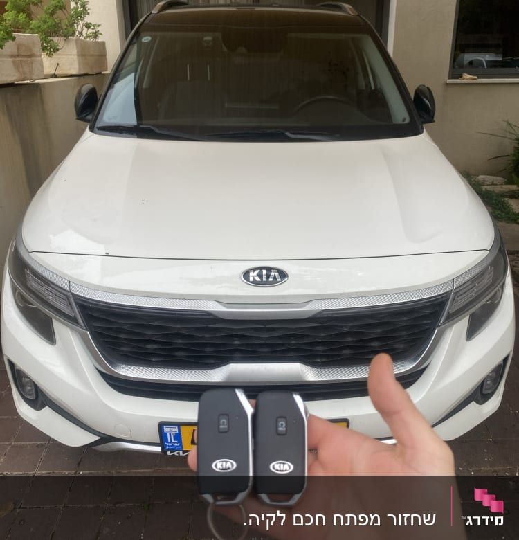 מפתחות רכב קיה מוחזקים מול רכב לבן